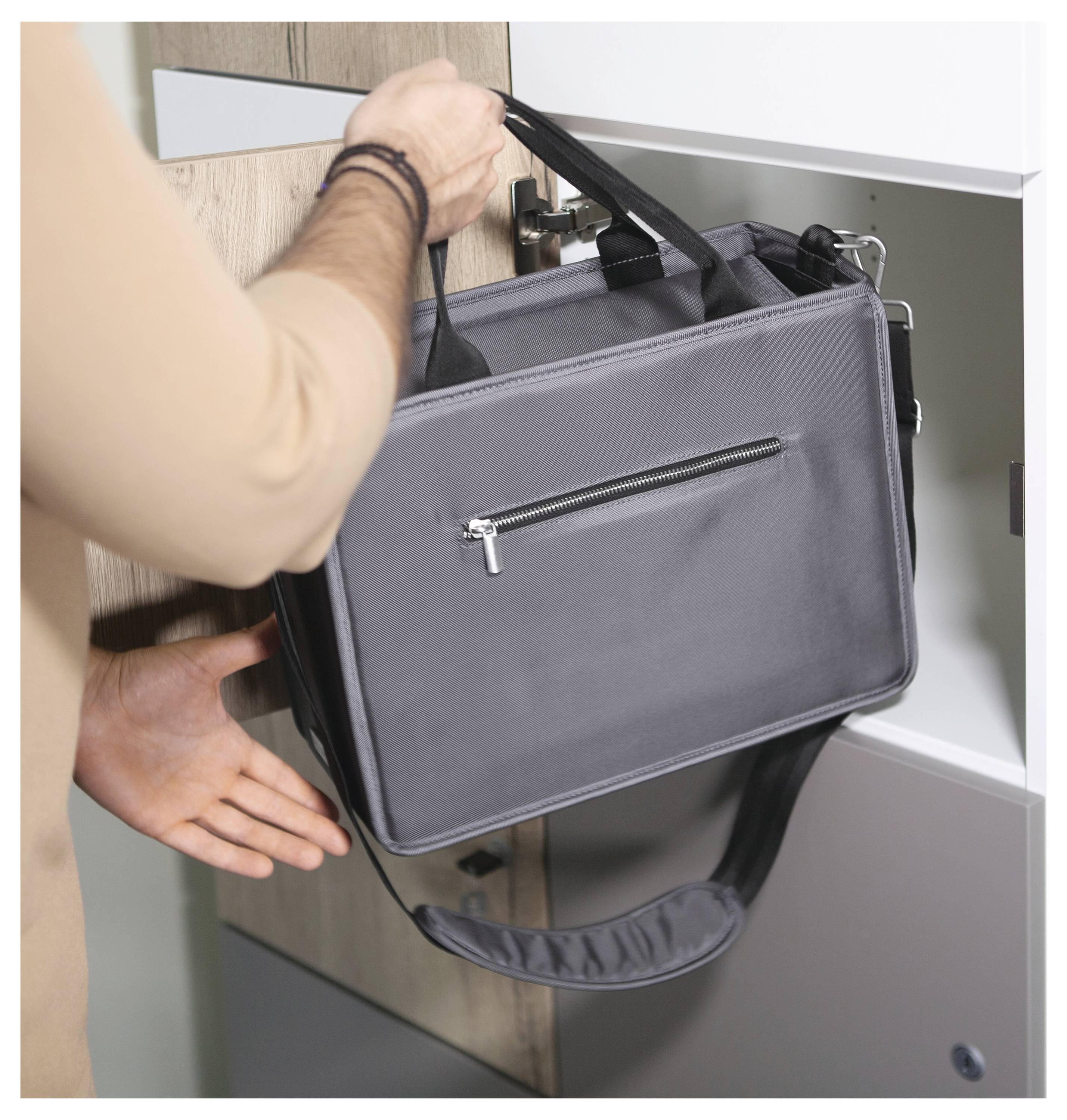 Person placing a gray shoulder bag into an open cabinet shelf.