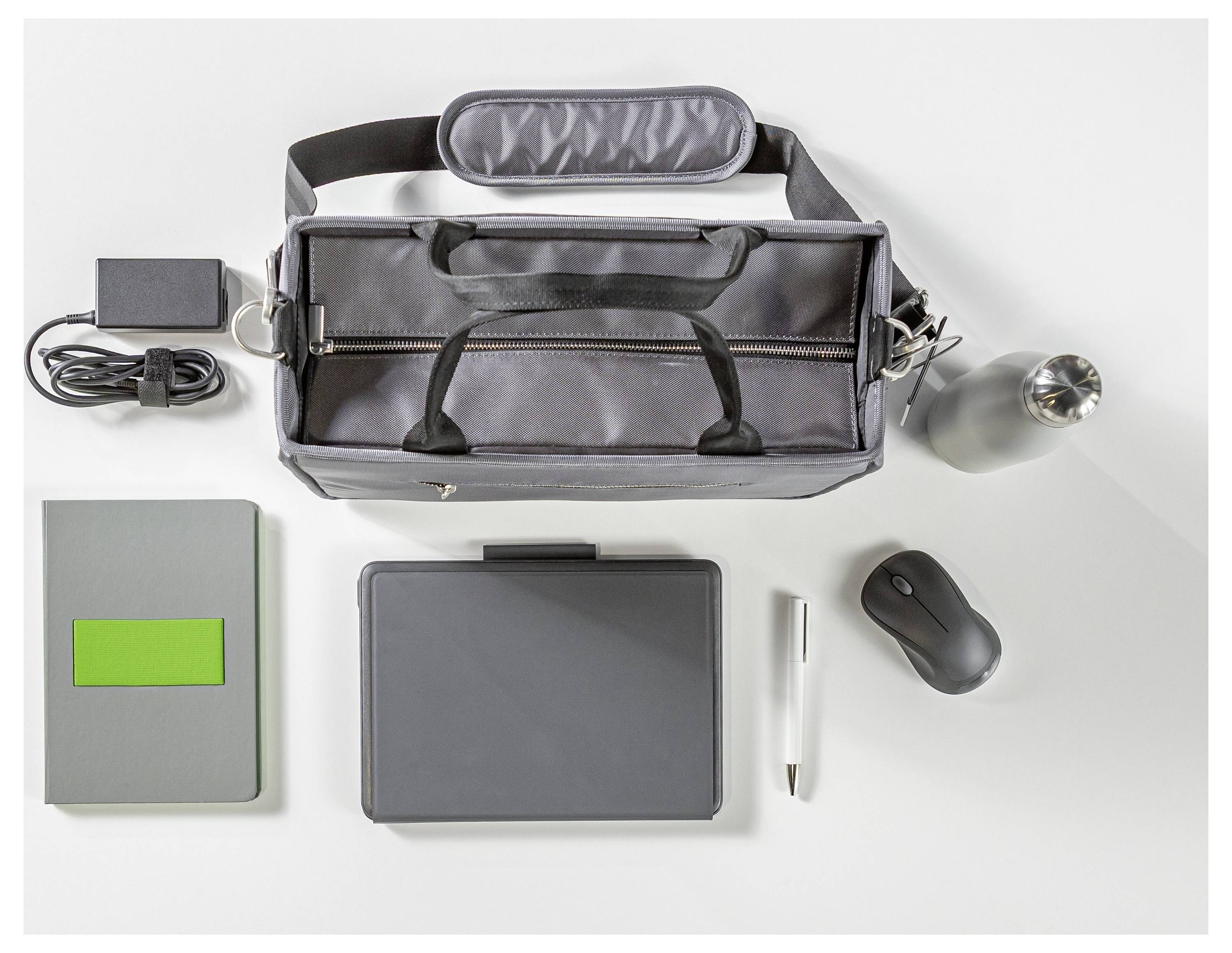 Flat lay of a gray laptop bag with charger, notebook, tablet, pen, mouse, and a metal cup on a white background.