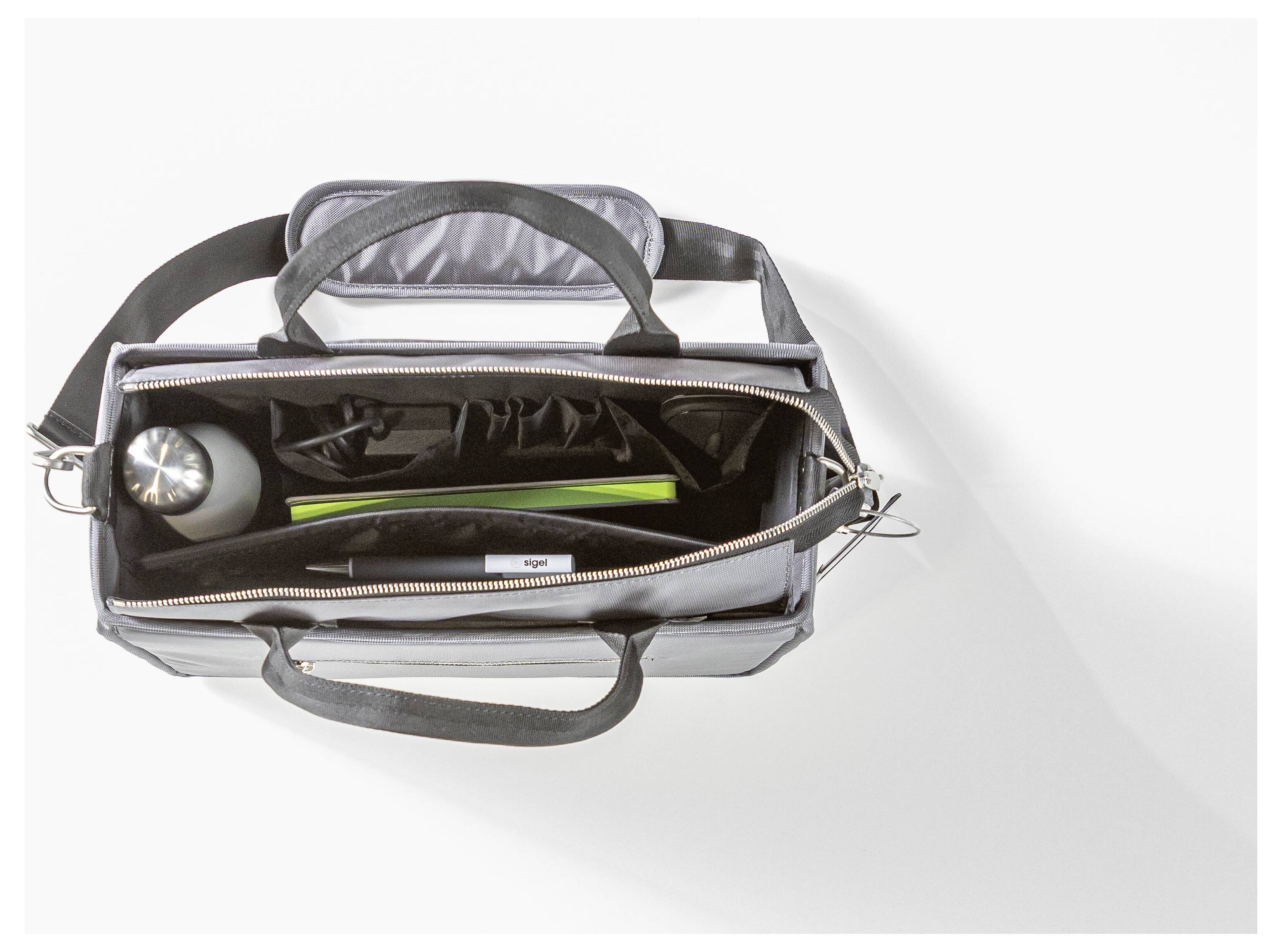 Open black bag viewed from above, containing a water bottle, black pouch, and a long, green object. It is placed on a white surface.