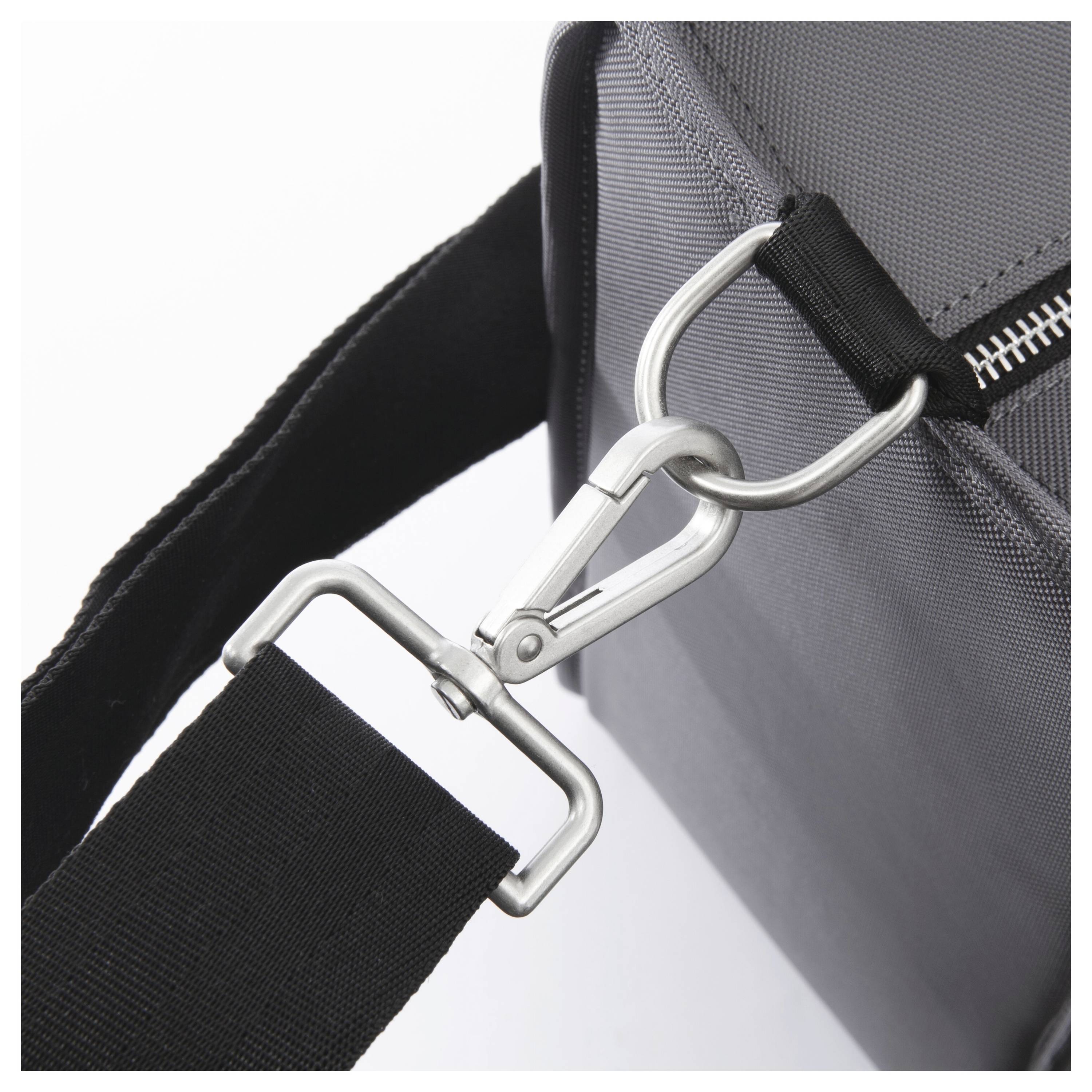 Close-up of a black shoulder strap clipped to a gray bag with a metal carabiner and ring attachment.