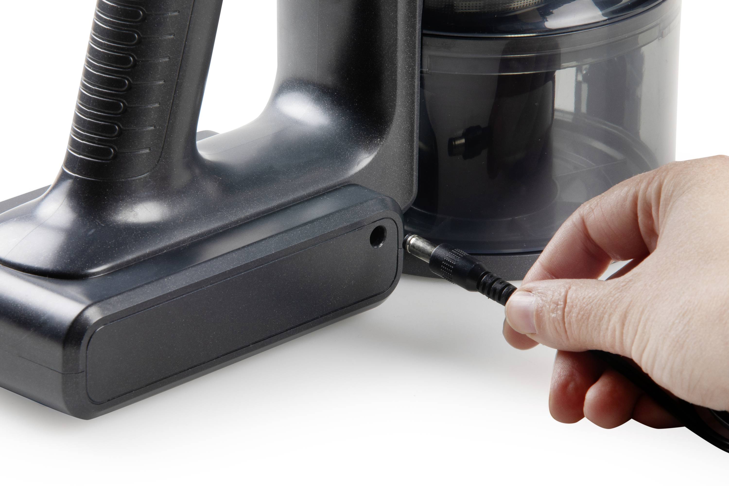 A hand plugs a charging cable into a cordless vacuum cleaner.