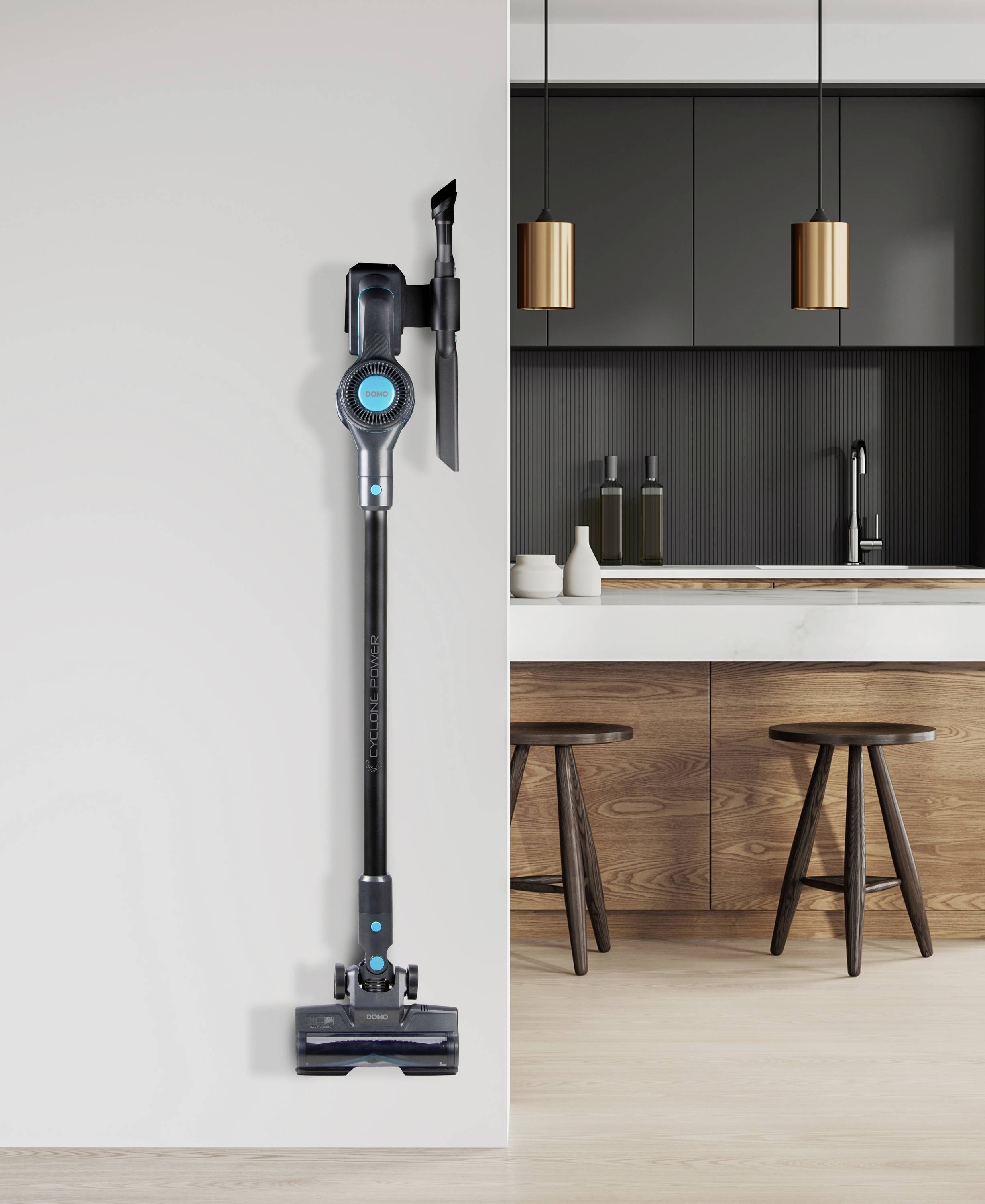 A cordless vacuum cleaner hangs on a wall mount in a modern kitchen with wooden bar stools and black cupboards.