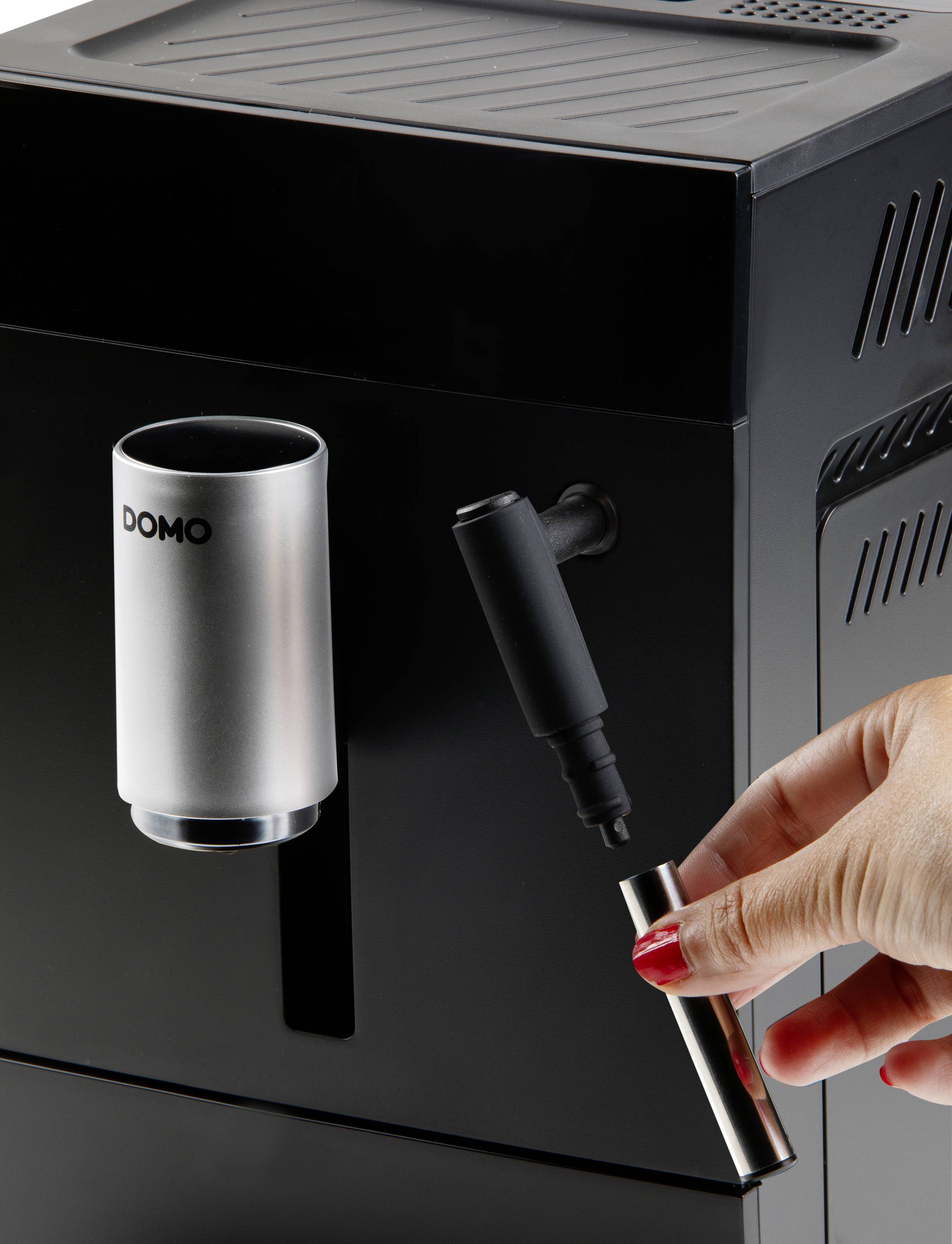 A black coffee machine with a silver jug. A hand is holding a metal pen close to the device.