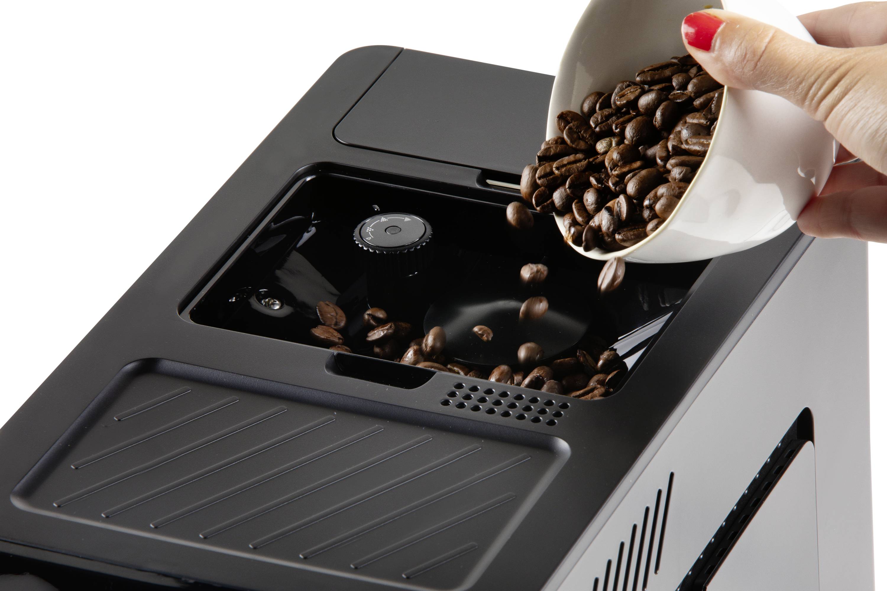 A hand is pouring coffee beans from a white cup into the container of a black coffee machine.