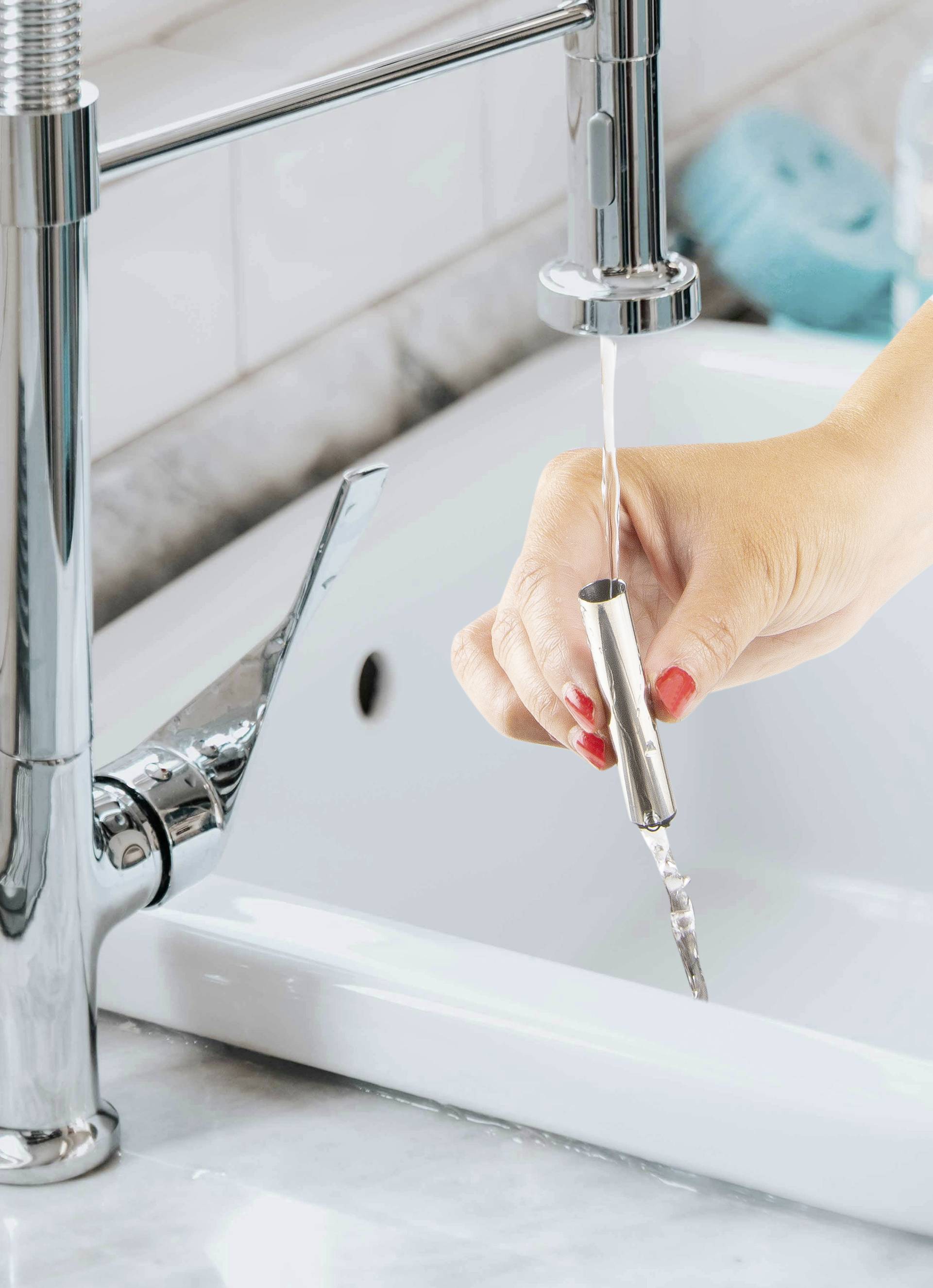 A hand holds a toothbrush under running water at the sink to clean it.