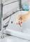 A hand holds a toothbrush under running water at the sink to clean it.