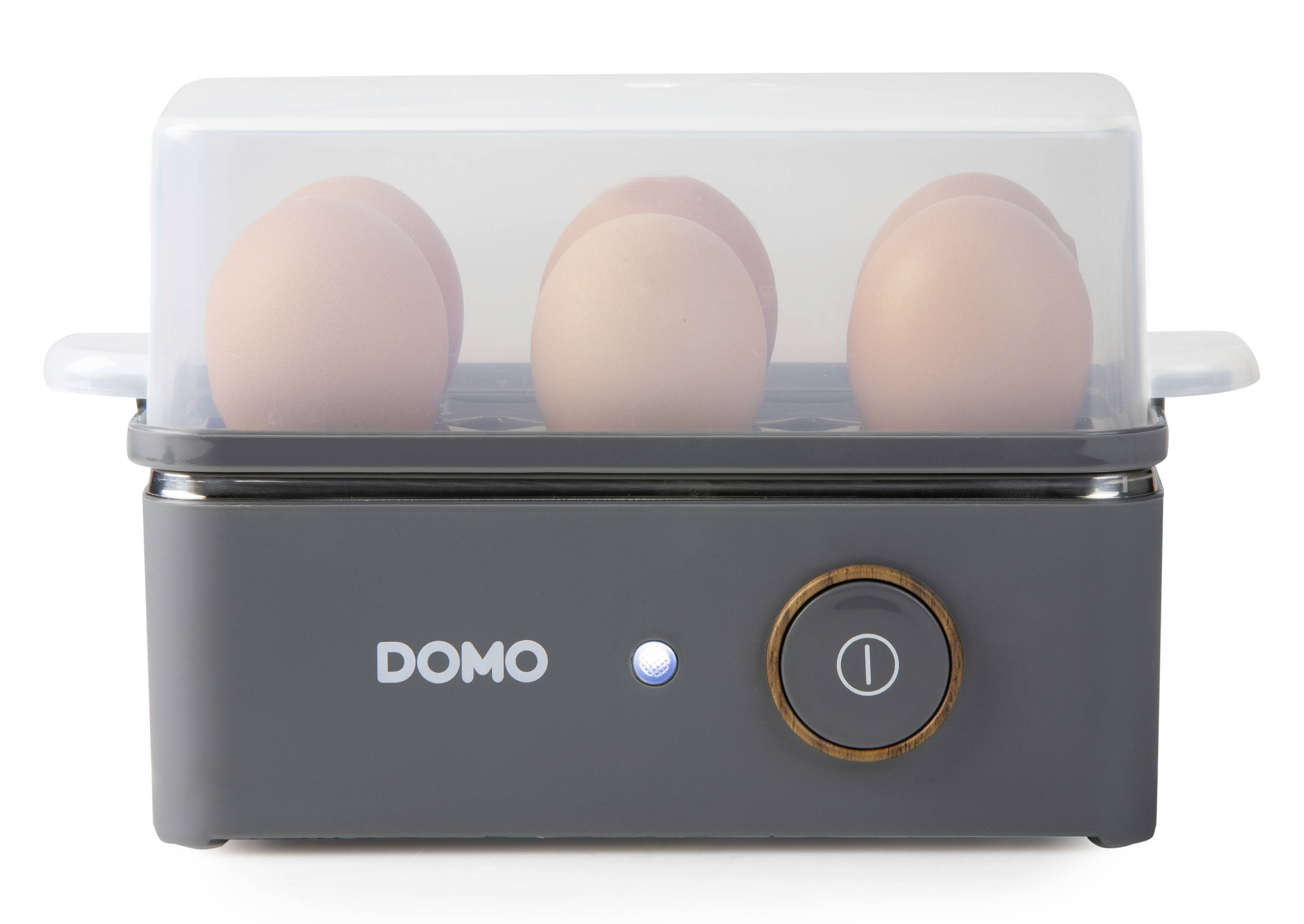 An electric egg cooker with a transparent lid shows three boiled eggs. The cooker is black with an on/off switch.