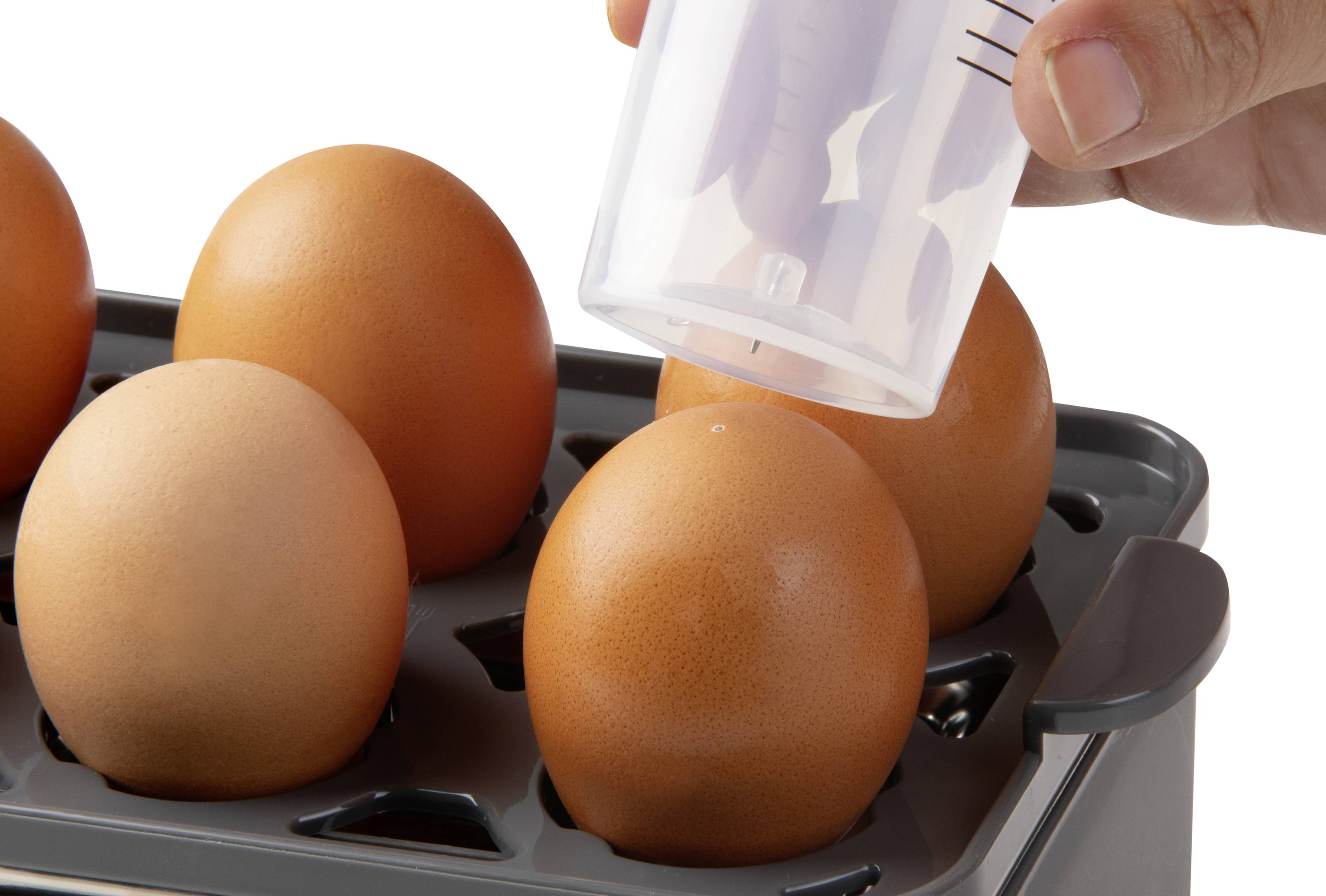 A hand is holding a container that pierces an egg at its tip. Several eggs in a holder.