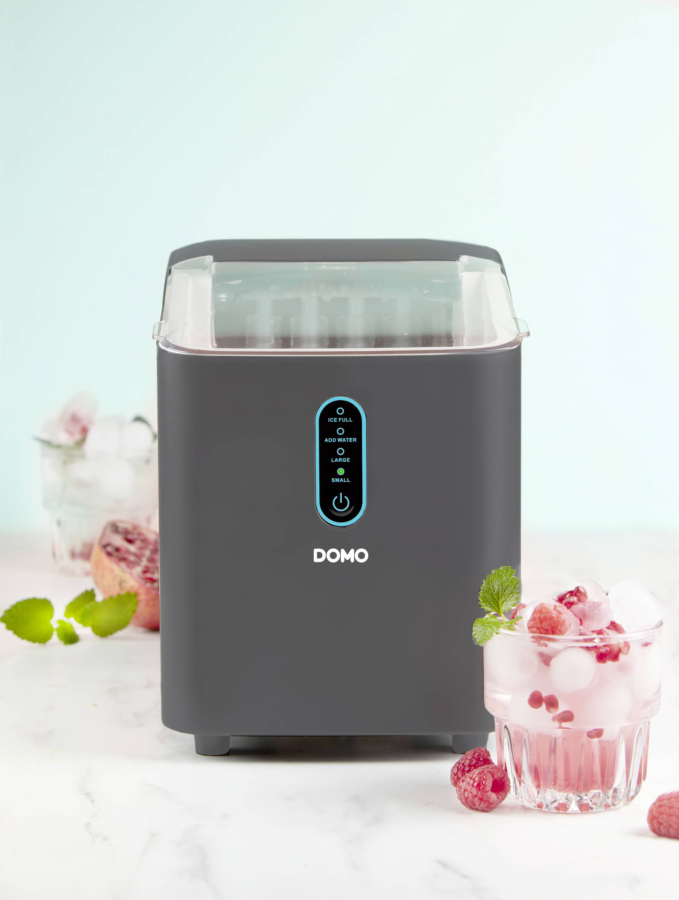 A black ice cream machine on a table with a glass of pink drink with ice and raspberries beside it.