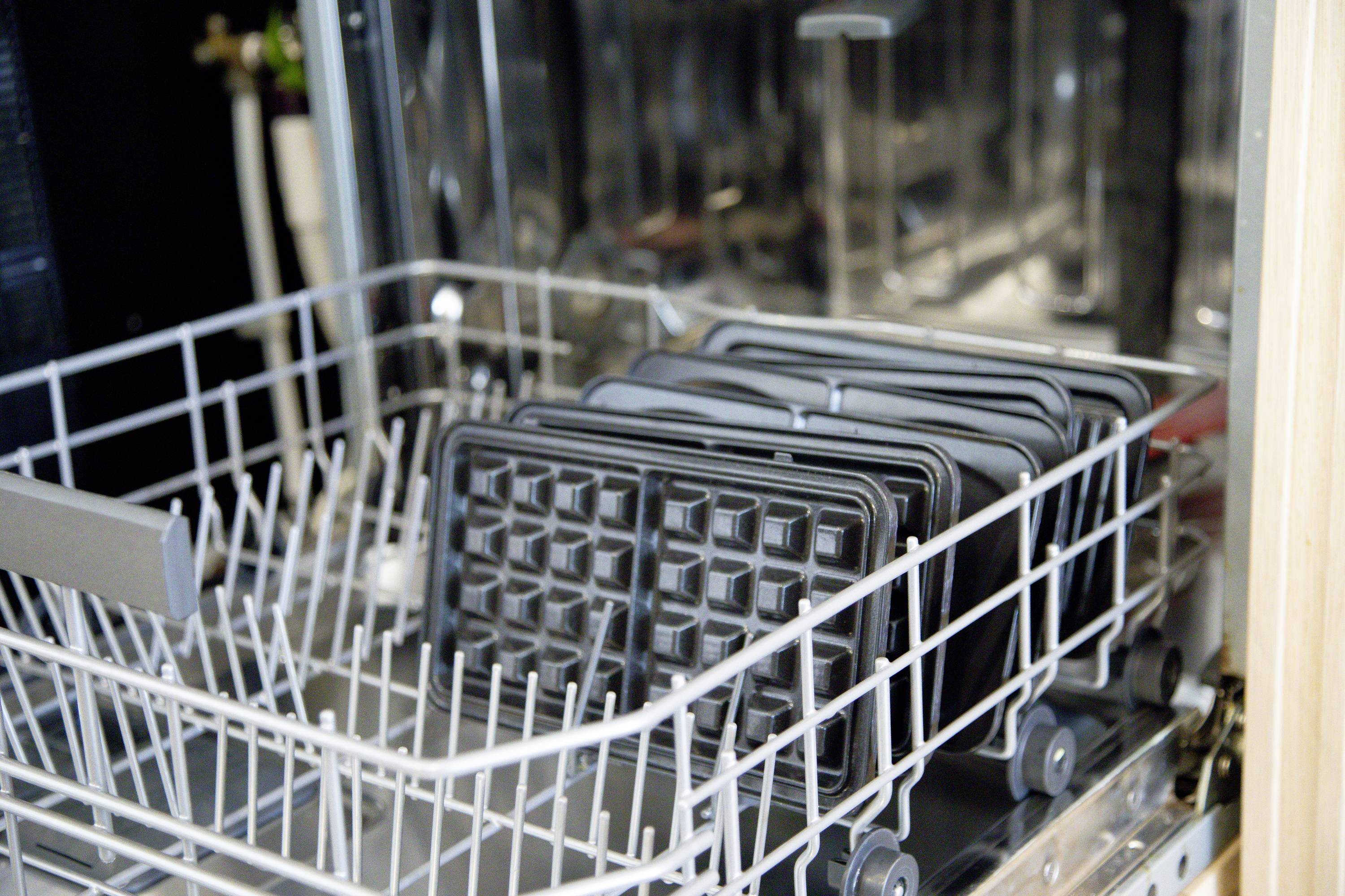 An open dishwasher with waffle iron plates arranged neatly in the top rack. The plates are clean and systematically placed.