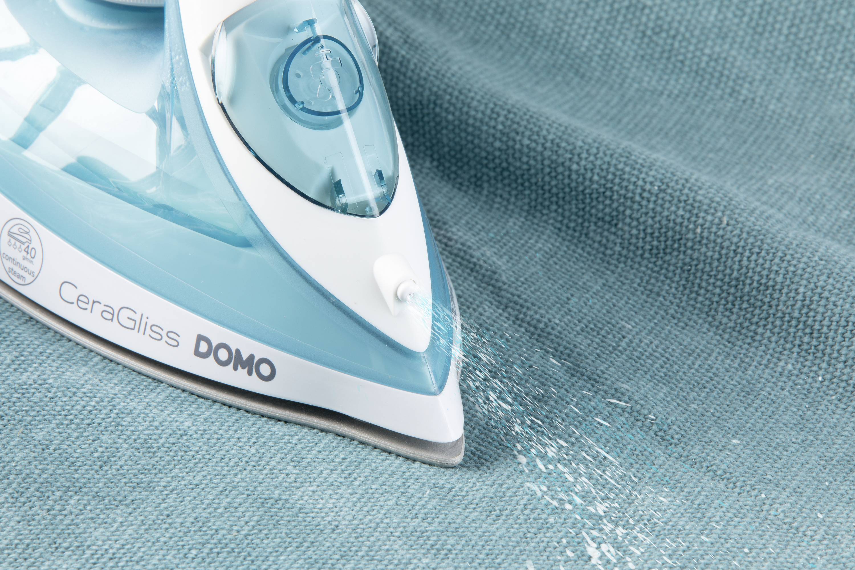 A blue iron smooths a blue cloth while steam emerges from the steam nozzle.