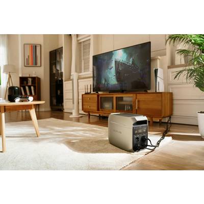 A portable power generator is standing in a living room. It is connected to an entertainment system. A film is playing on the television in the background.