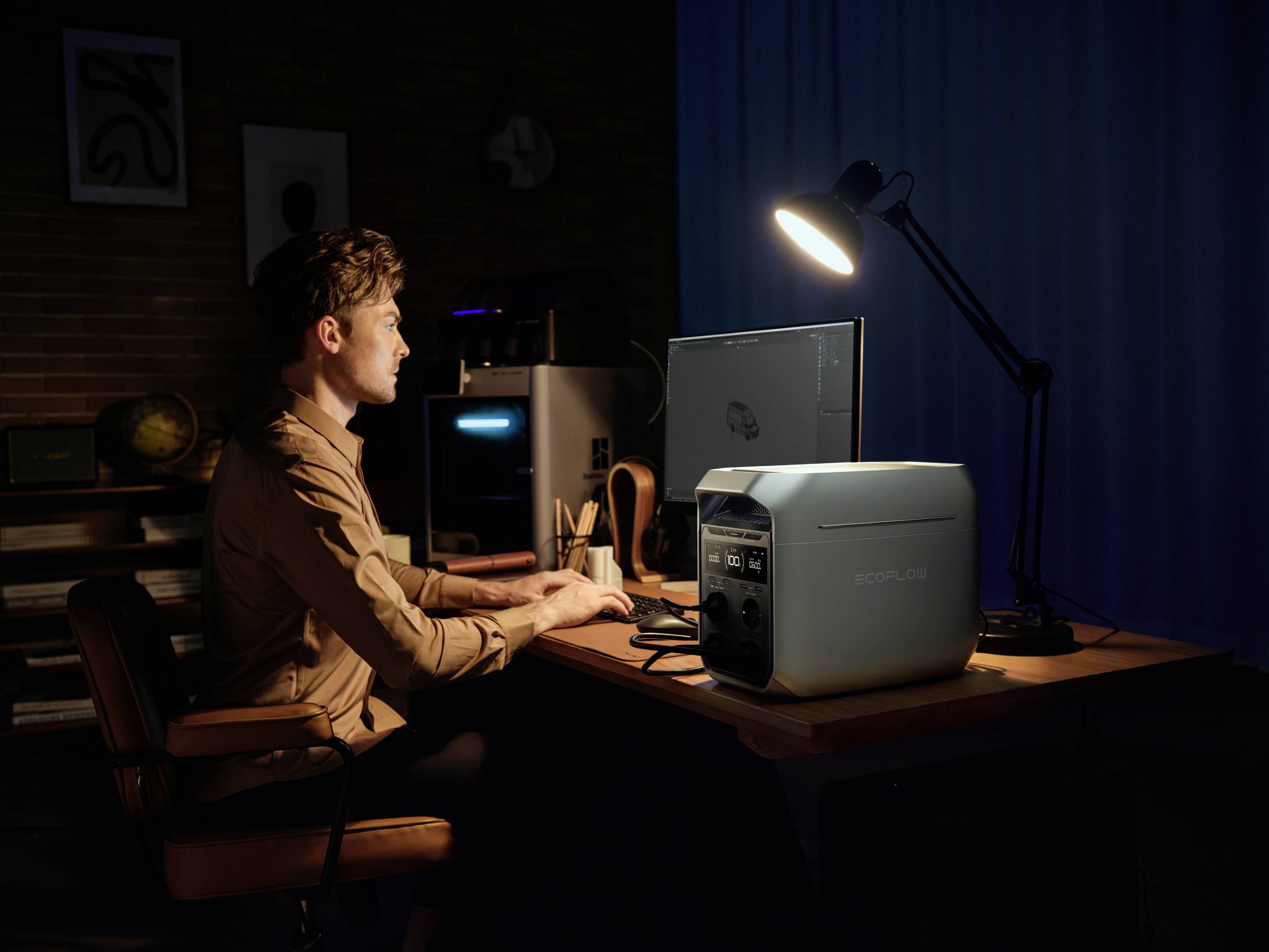 A person is sitting in a dimly lit room at a desk, working on a computer with a lamp and a portable generator on the table.