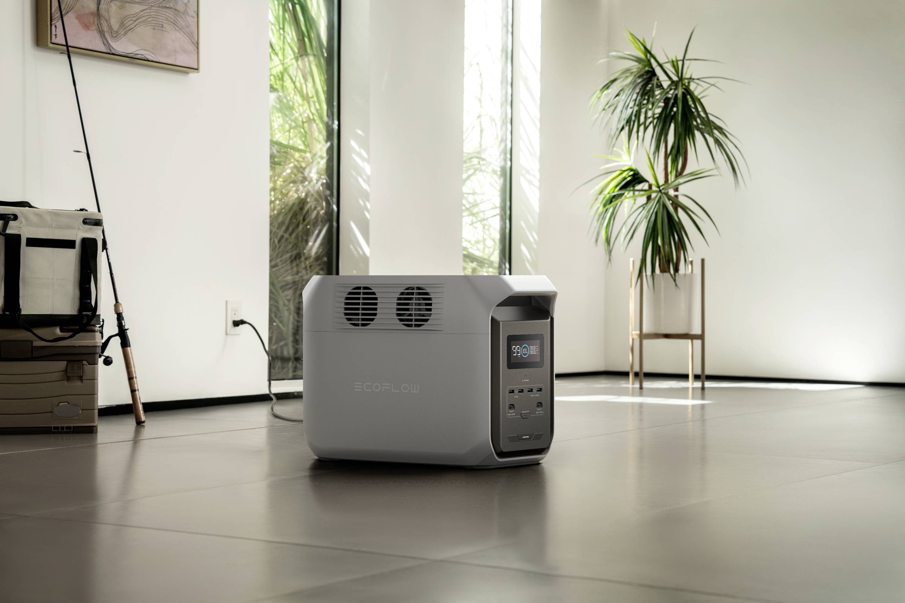 Grey portable power generator sits on the floor of a modern, bright room with large windows and plants in the background.