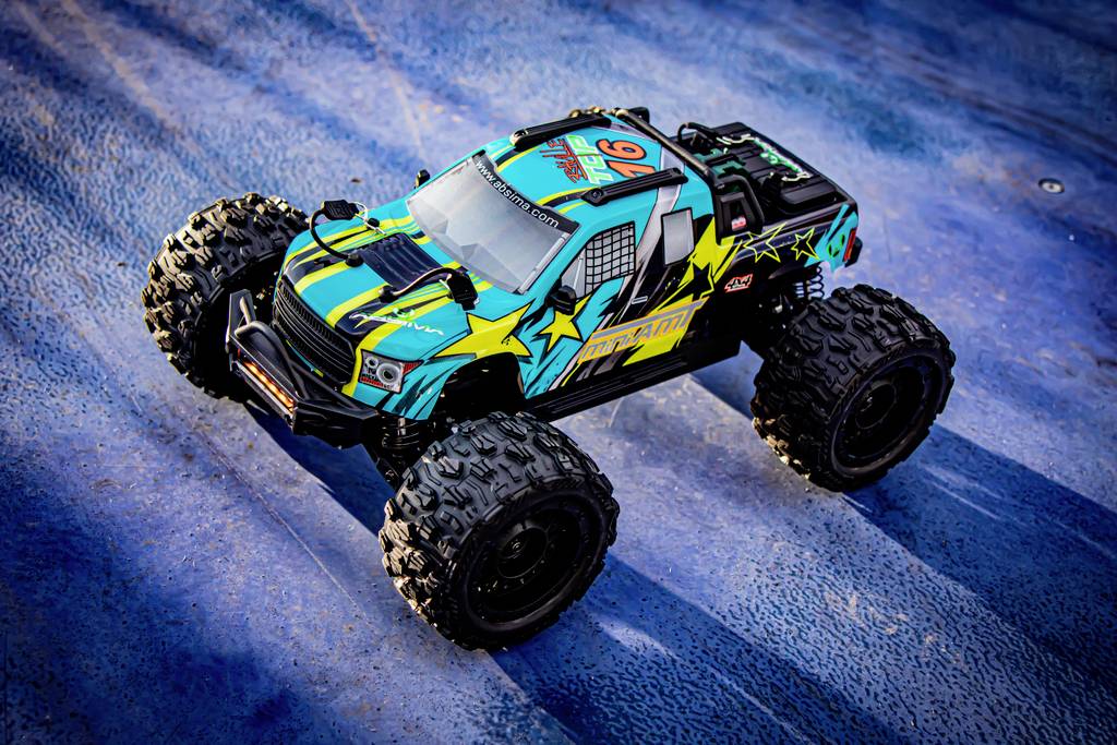 A colourfully designed remote-controlled car with large tyres drives across a blue-coloured surface.