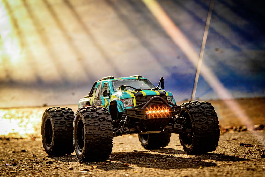 A remote-controlled car on a dusty surface. It is illuminated by sunlight and shows large, robust tyres.
