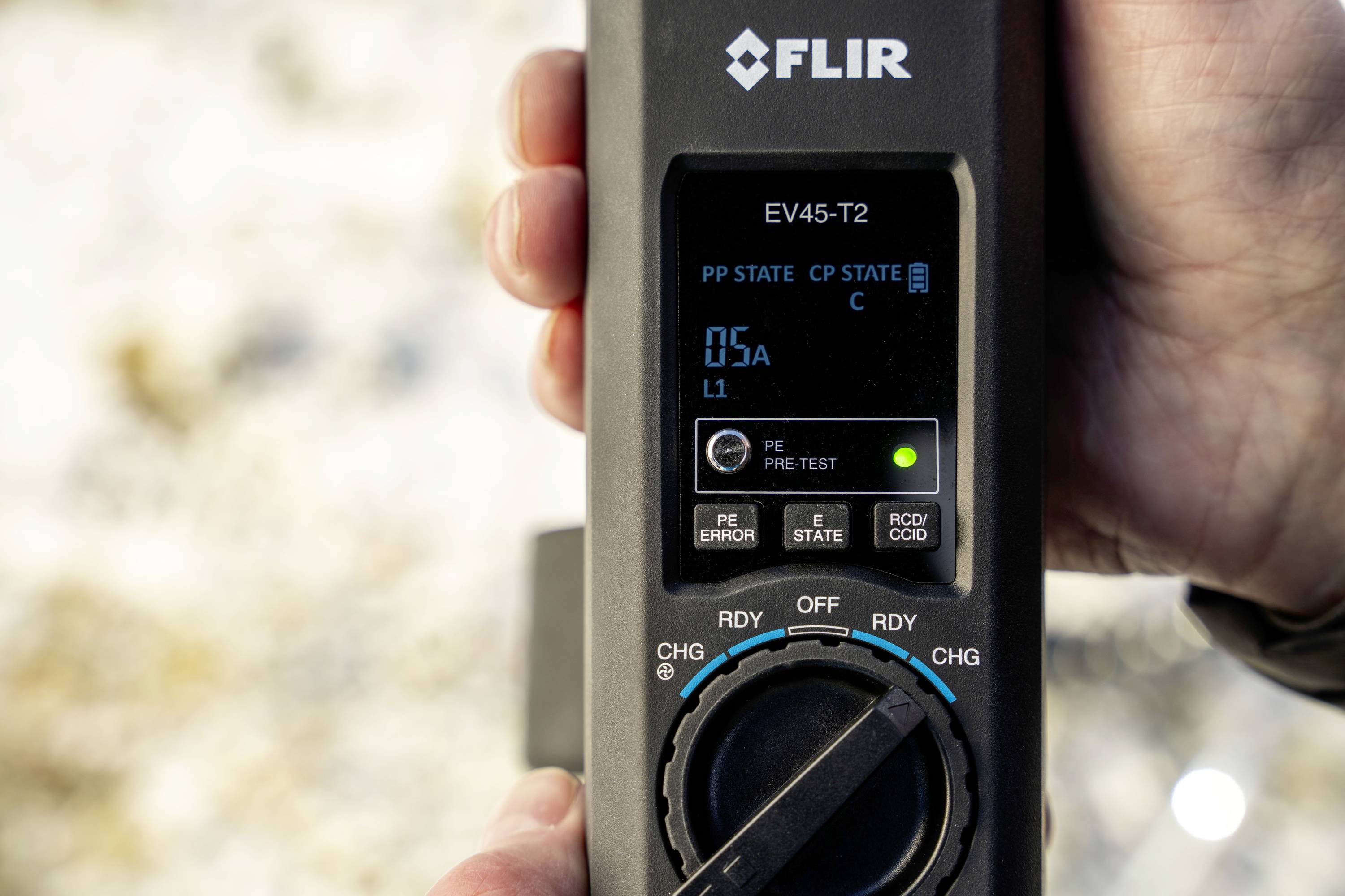 A hand is holding a FLIR EV45-T2 device showing 0.5A. The display shows status information and various operating modes.
