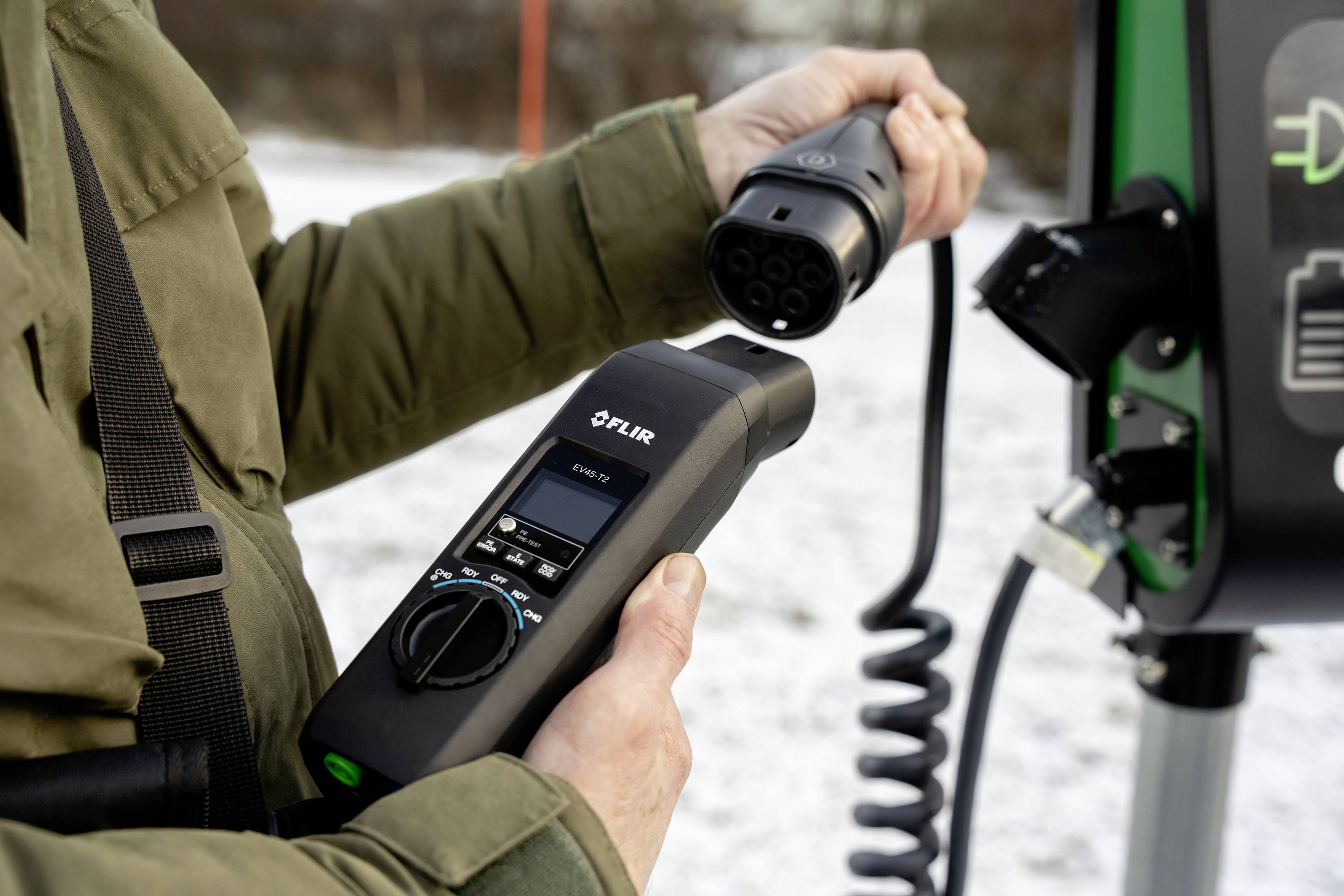 A person is charging an electric car at a charging station. They are holding a charging cable and connecting it to the station.