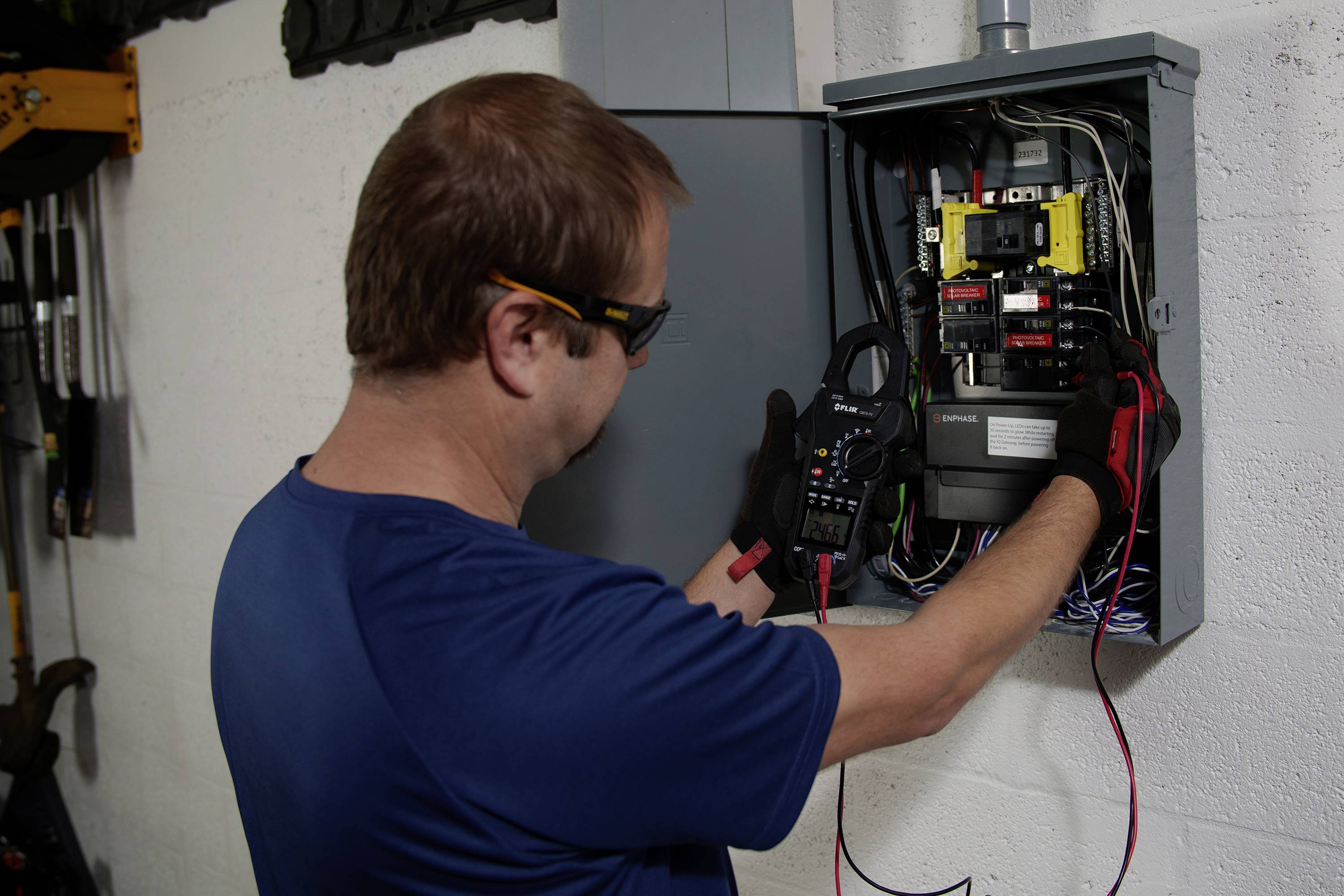 A technician is working on an open fuse box, checking electrical connections using tools and equipment.