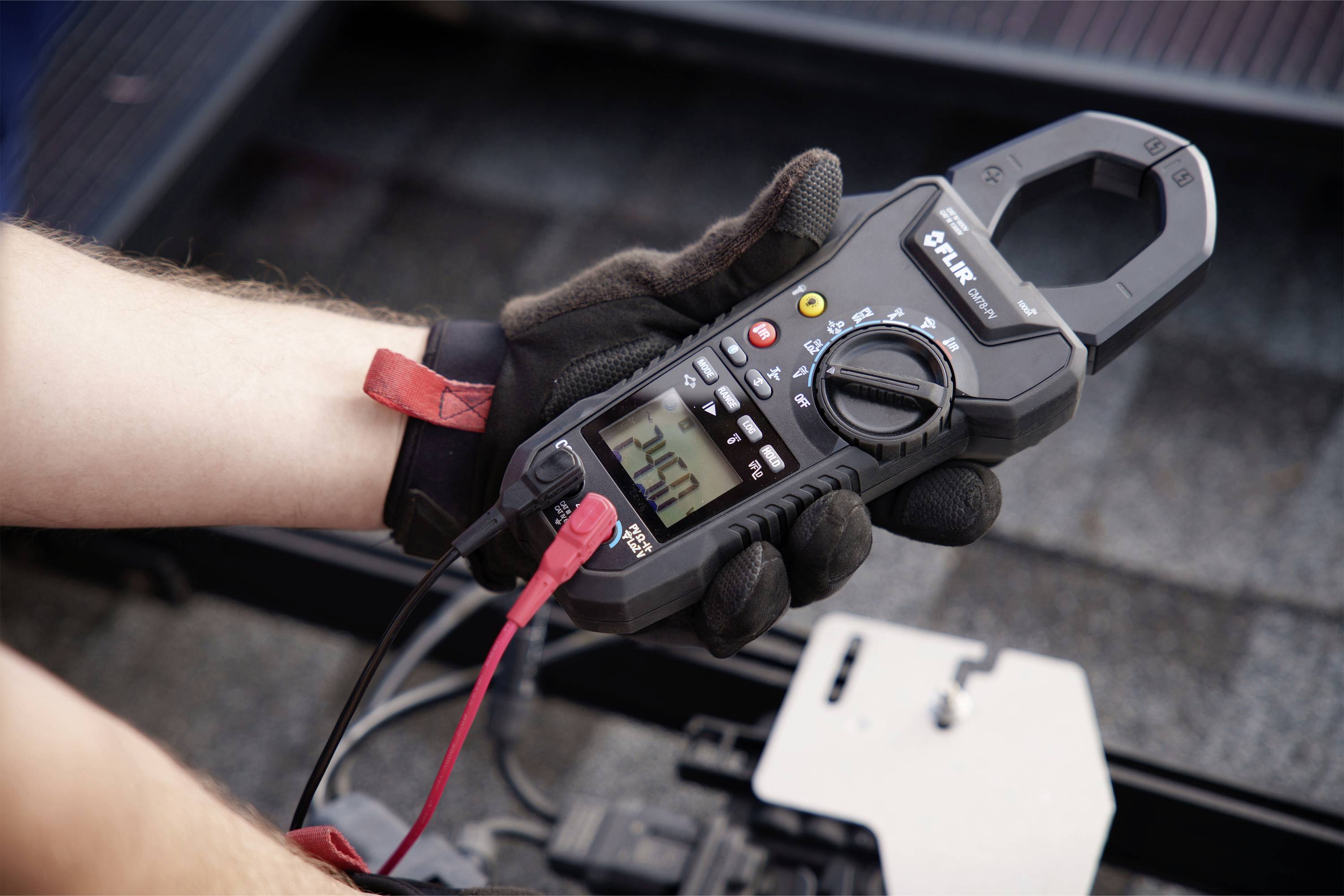 A person is holding a digital multimeter displaying 245.0. The device is being used for measurements on an electrical system.