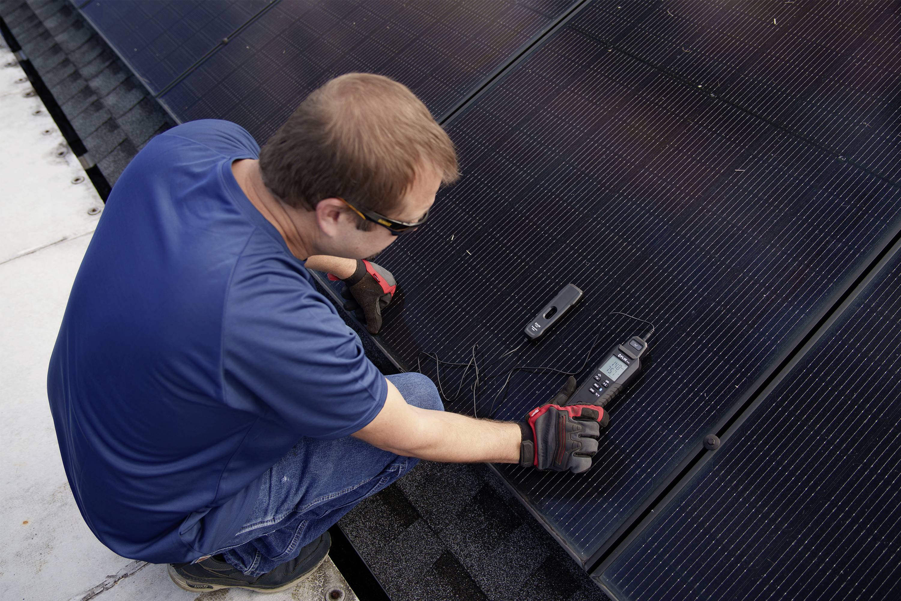 A person is checking the performance of solar modules on a roof using a measuring device.