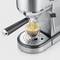 'Espresso machine brewing fresh espresso in a glass beaker, silver design with steam nozzle. Coffee flowing from double spout.'