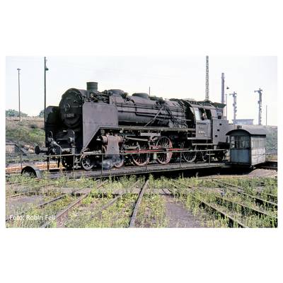 An old steam locomotive on a triangle of railway tracks, surrounded by railway lines and vegetation. A small shed stands nearby.