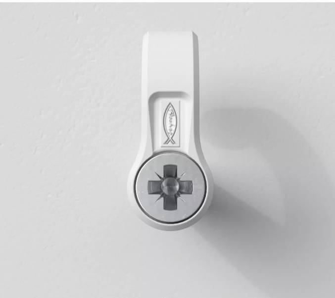 A white wall hook with a screw fastening, mounted on a light grey wall. A fish symbol is located at the top.