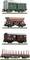 Four model railway wagons in a row: a green goods wagon, a red bulk carrier, a red covered wagon, and a red flatbed wagon.