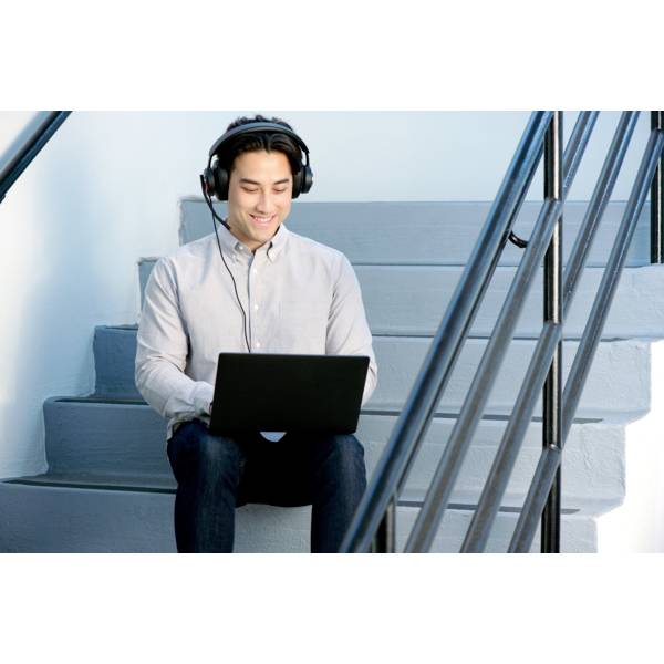A man wearing headphones sits on a staircase, working on a laptop and looking focused.