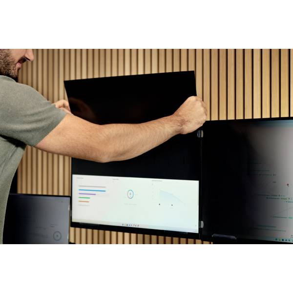 A person is hanging a large screen on the wooden wall. Next to the screen is a smaller monitor displaying diagrams and data.
