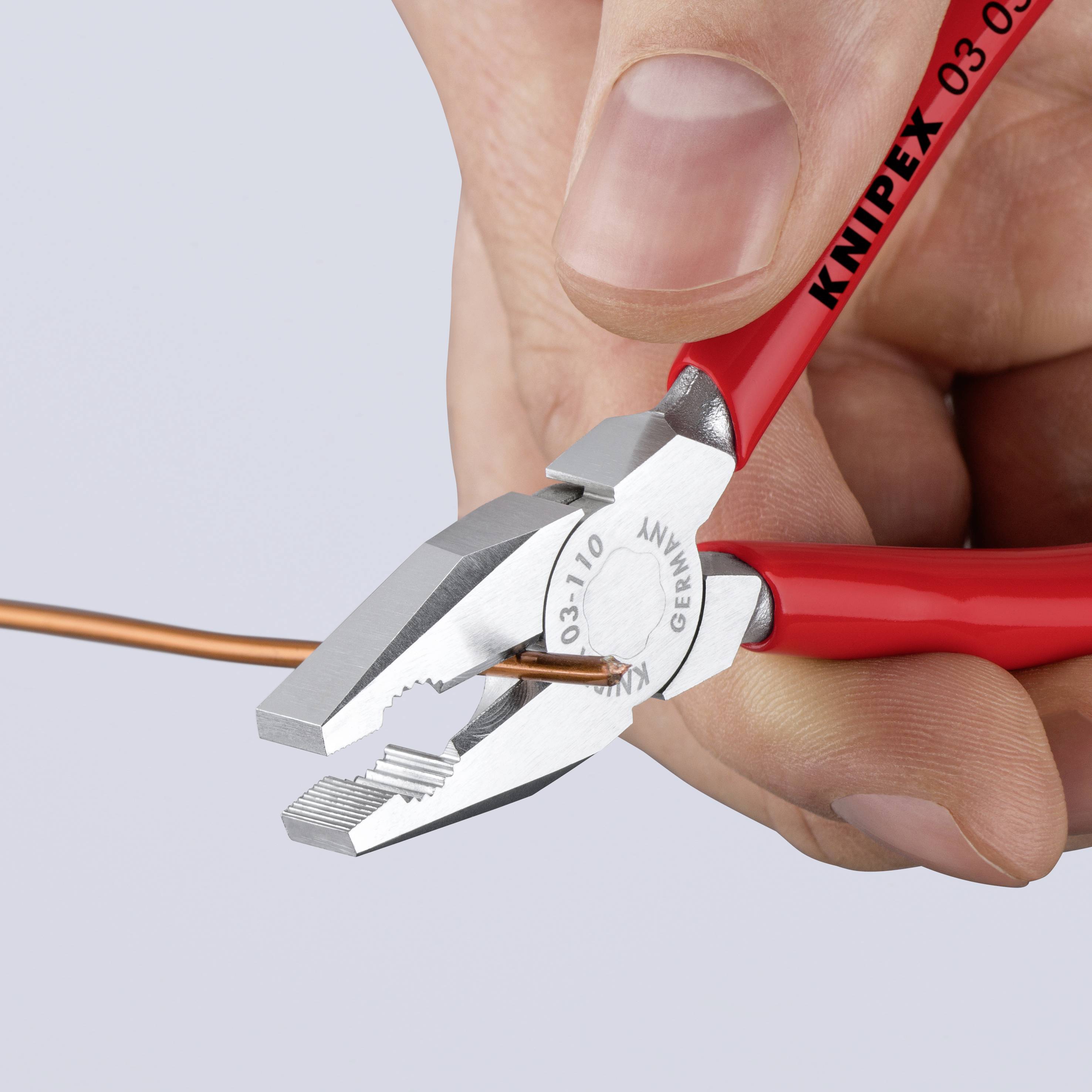 A pair of red pliers cuts a thin, orange cable. A hand grips the pliers firmly.