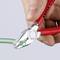 A red pliers cuts a green cable. 'KNIPEX' is written on the pliers. A hand is holding the pliers.