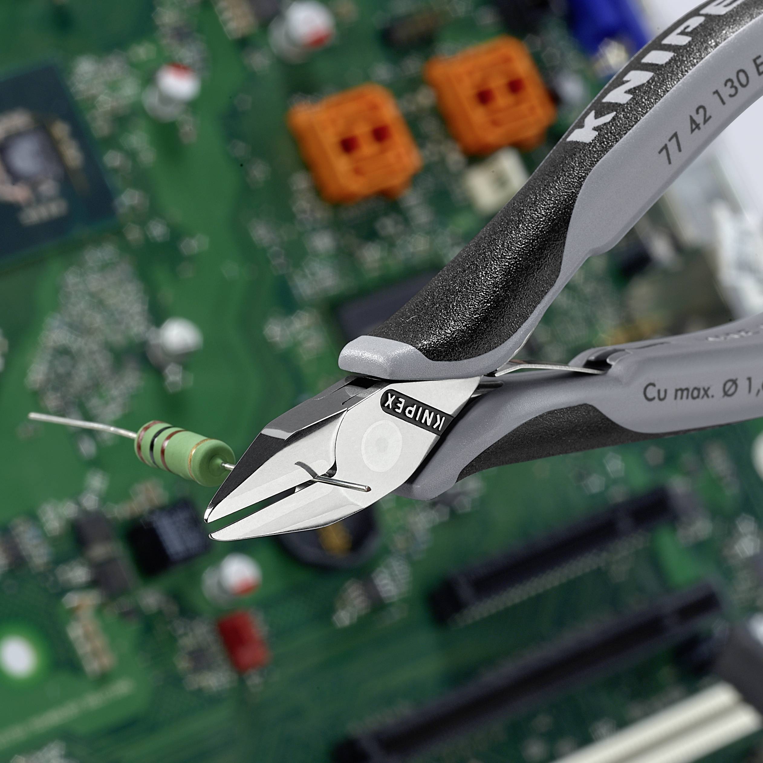 A side cutter is cutting a wire above a green circuit board. Electronic components are visible in the background.