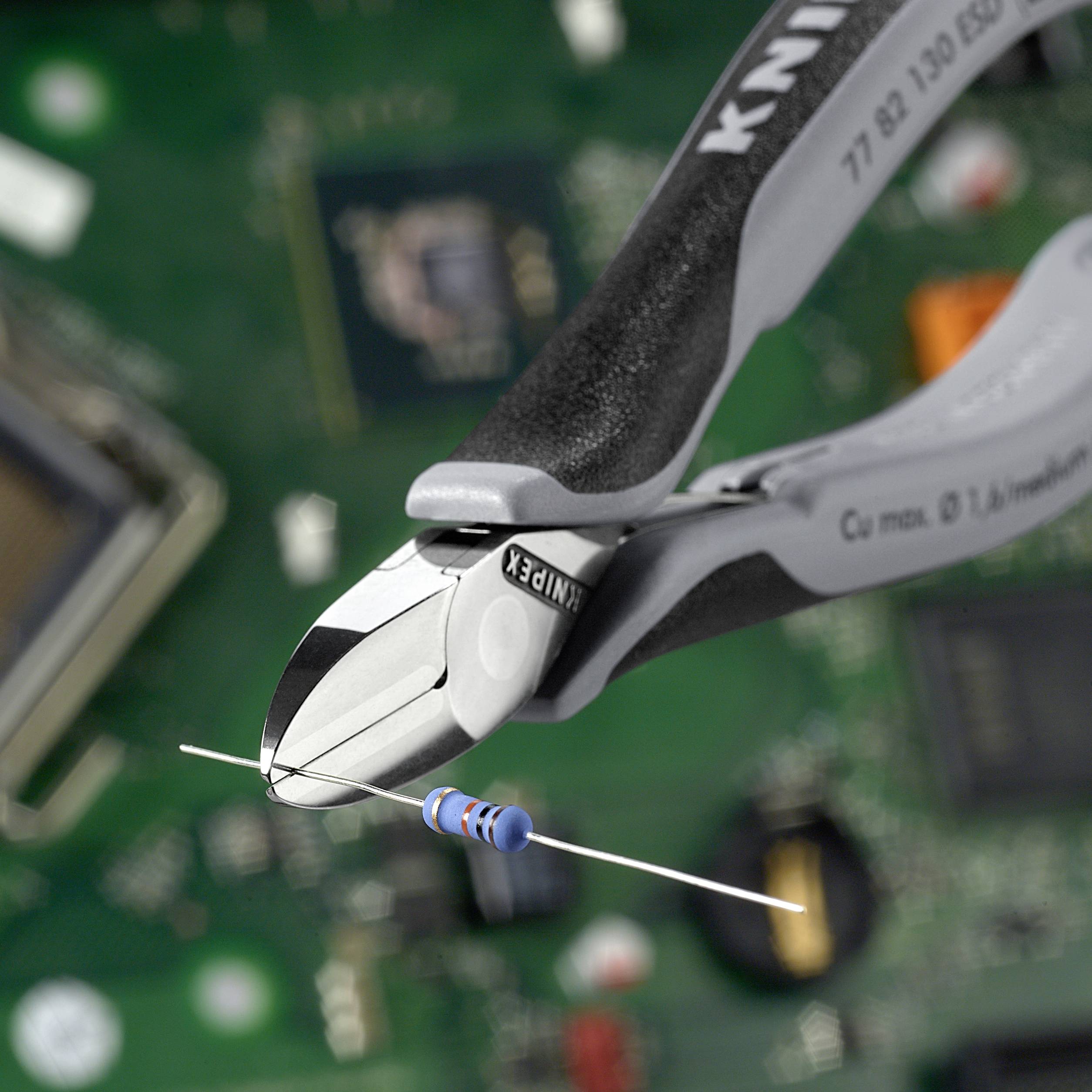 A pliers cuts an axial resistor over a green circuit board. Electronic components are blurred in the background.