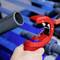 A red pipe cutter cuts a grey plastic pipe. Background blurred, blue and grey tones dominate. A worker's hand holds the pipe.