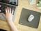 A hand is typing on a laptop, with a computer mouse on a mousemat on a wooden desk, surrounded by office supplies.