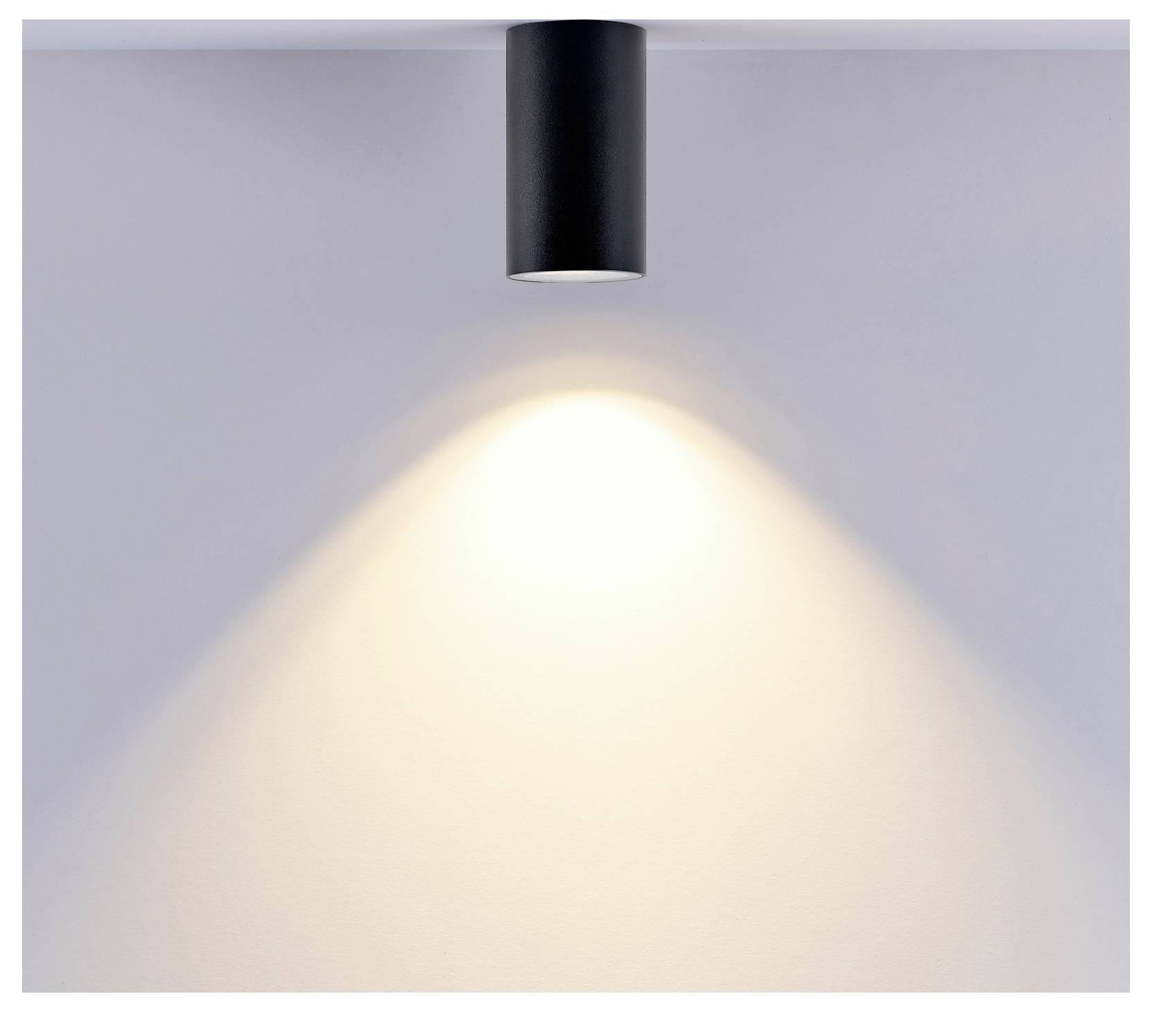 Black ceiling spotlight casting a warm cone of light on a gray wall.<br>