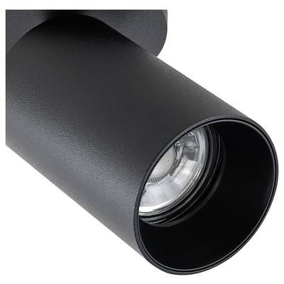 A black cylindrical ceiling light with a visible LED spot, mounted on a room ceiling, provides targeted illumination.