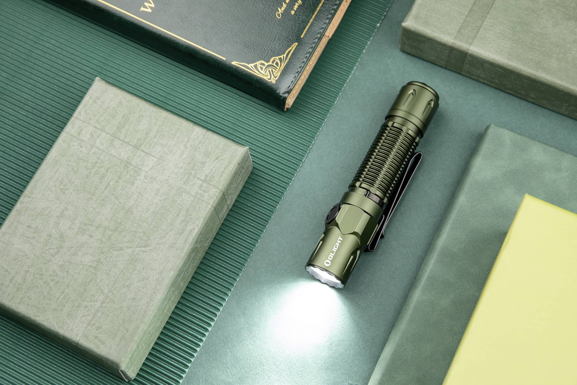 A green torch beams light onto a green surface. Surrounded by books, it is centrally positioned and illuminating.