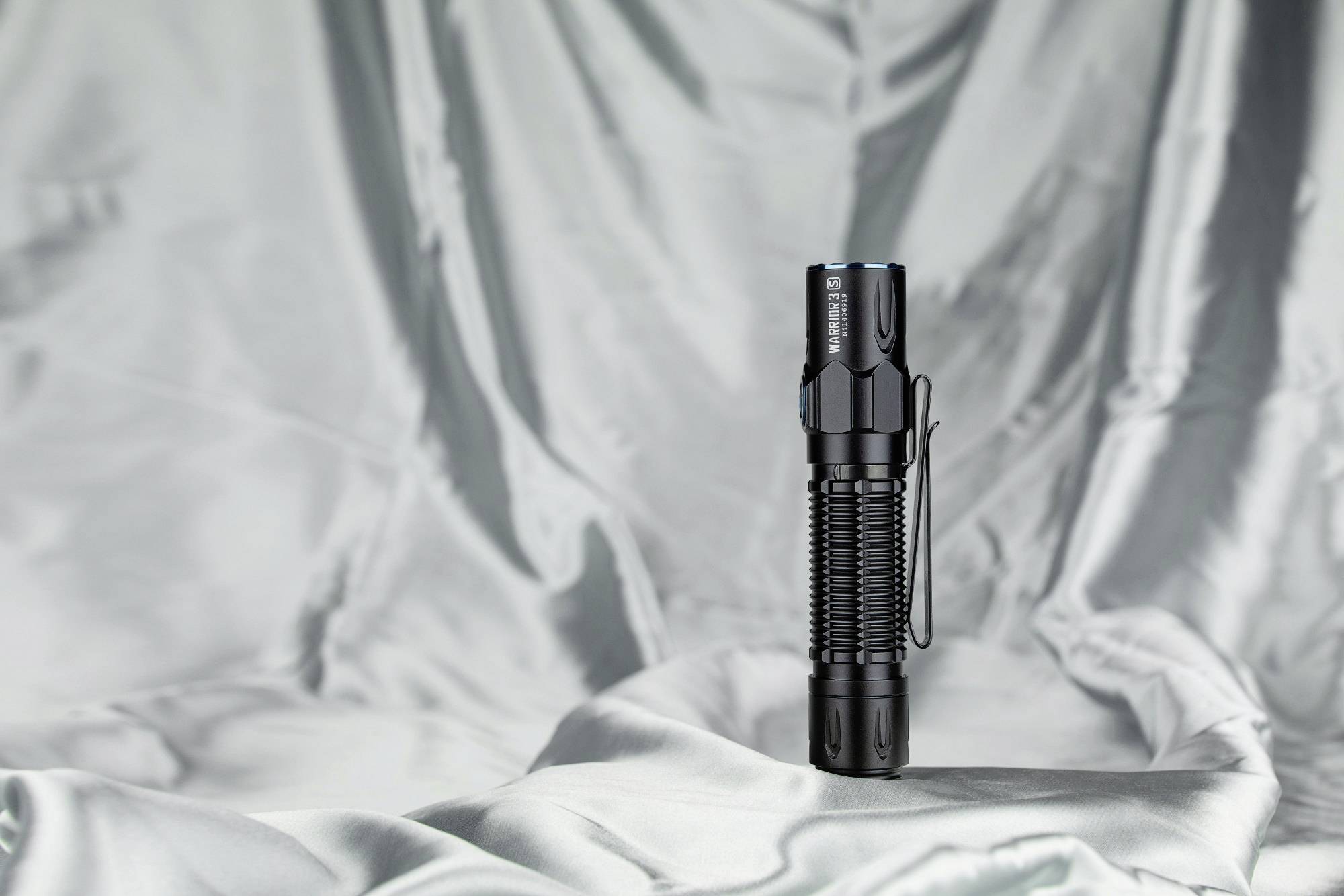 Black torch stands on a silver, shiny fabric background. It has a clip on the side and appears sturdy.