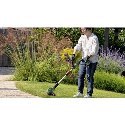 A person is trimming the edge of a lawn with a lawn strimmer. They are wearing safety glasses and gloves. Background with colourful plants.