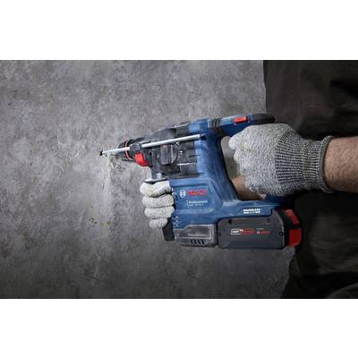 A person is drilling into a concrete wall with a blue Bosch cordless hammer drill. They are wearing grey work gloves for safety.