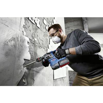 A person is wearing safety glasses and a mask while drilling into a concrete wall with a power drill.