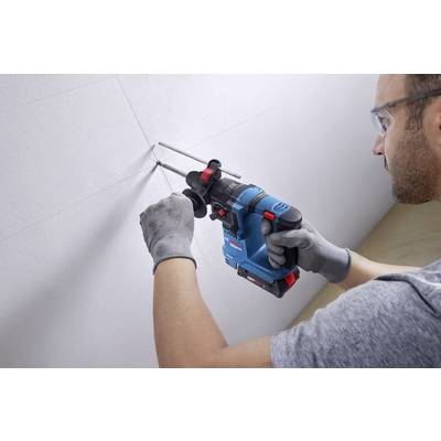 A man is drilling holes in a white wall using a blue drill. He is wearing safety glasses and gloves for protection.