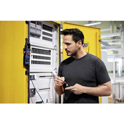 A man is working on an open electrical cabinet. He is holding a tool and inspecting the electrical components inside.