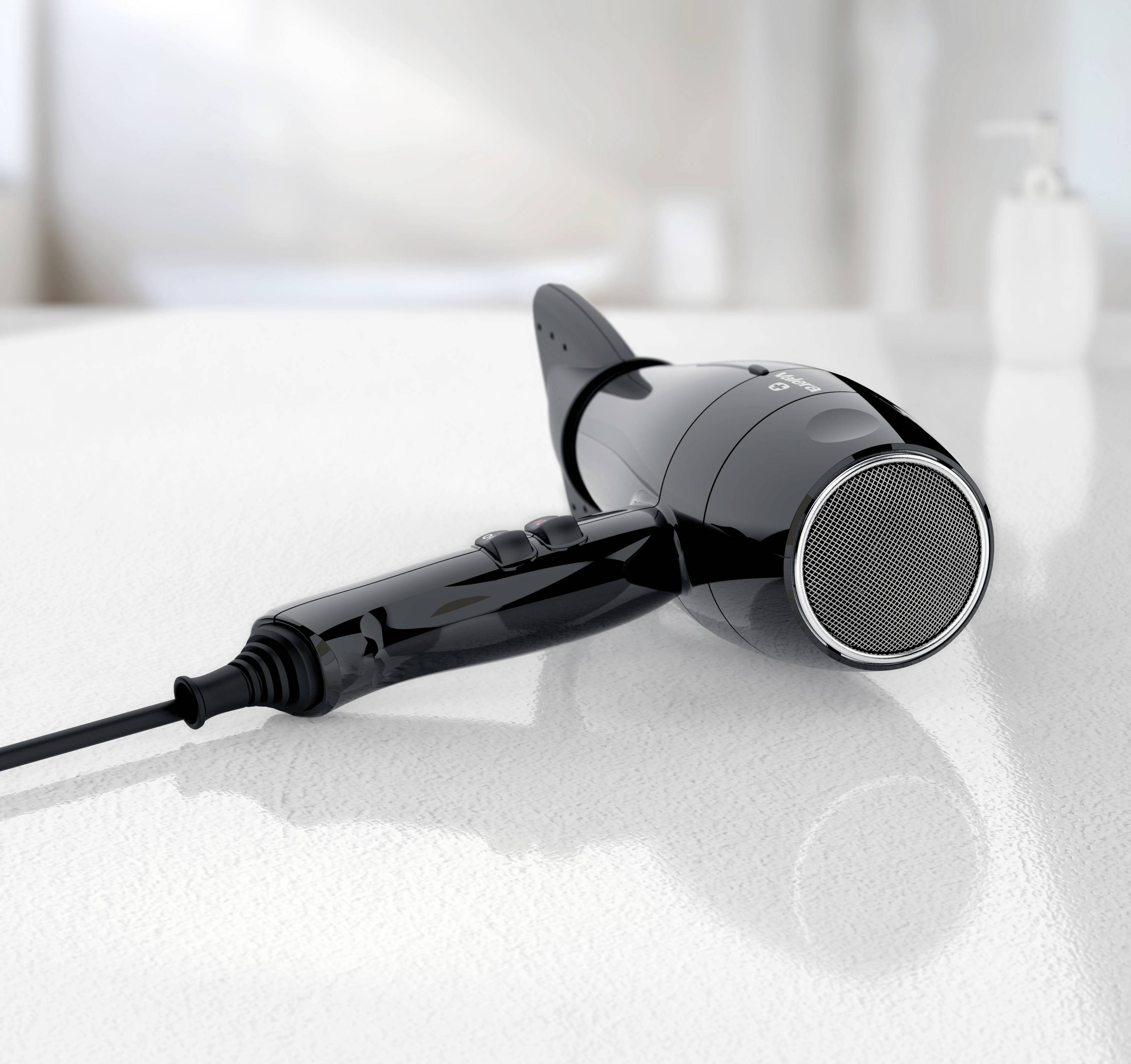 Black hairdryer on a white table, with power cable. Blurred background shows a sink area.