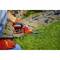 A person is cutting grass with red garden shears beside a stone path. They are wearing red gardening gloves and sitting on the ground.