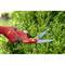 A hand wearing a red glove uses red garden shears to trim a hedge. The secateurs bear the logo of a garden tool brand.