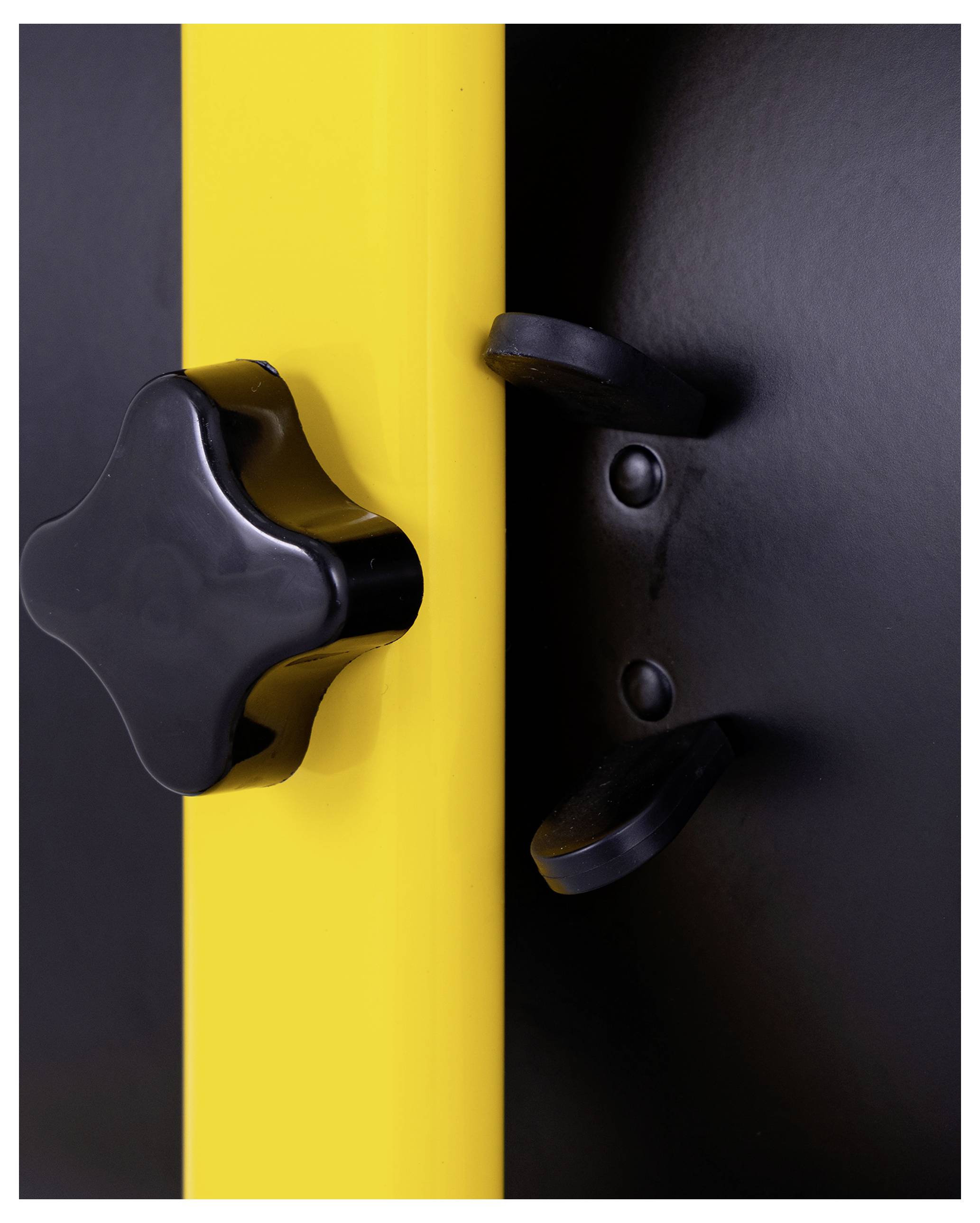 'A close-up of a black knob on a yellow panel, with two black metal latches next to it, possibly part of a secure locking mechanism.'